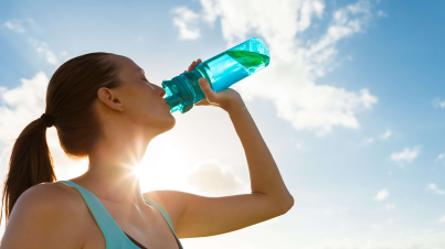 donna runner al sole che beve da una bottiglia dopo una corsa